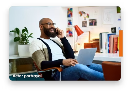 A smiling man sits in a chair with a phone to his ear and a laptop on his lap representing an MS patient discussing MAVENCLAD® (cladribine) treatment with their doctor. Not a real patient.